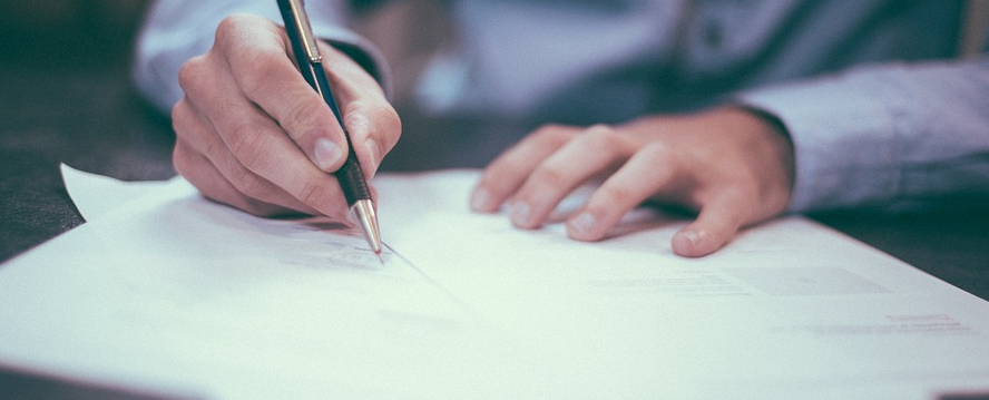 A person writing on a piece of paper with a pencil.